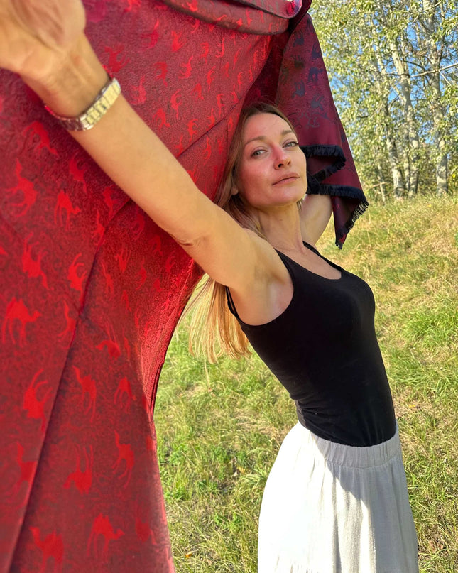 Czerwona chusta jedwabna z żakardowym wzorem karawany na tle natury, kobieta prezentująca szal