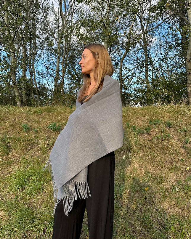 Kobieta owinięta luksusowym szarym szalem kaszmirowym na tle natury
