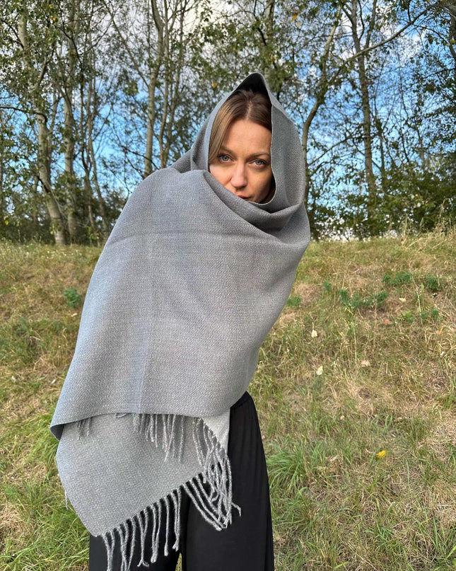Szary szal kaszmirowy o delikatnym splocie i frędzlach otulający kobietę na tle natury